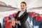 Joyful flight attendant standing near passenger seat in airplane