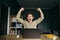 Joyful freelancer in a shirt sits at a desk with a laptop and emotionally rejoices with his hands up. Portrait of a happy young