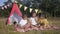 Joyful friends kids show funny faces and play with book on picnic on background of bigwam during weekend in forest