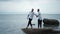 A joyful gay couple has fun dancing on a rock in shallow water holding hands with laughter during their honeymoon