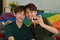 Joyful gay couple taking a selfie with compact camera in living room rainbow flag in background. LGBT, love and human