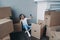 Joyful girl chatting by video call sitting with cardboard boxes during packing things for relocation