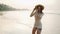 Joyful girl in flowery dress running, posing at tropical beach in sunrise light. Young pretty woman in straw hat has fun