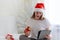 Joyful girl in santa hat is sitting on the bed