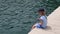 Joyful girl with spinner sits on pier near sea hanging her legs. Little girl playing with her feet and singing songs