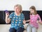 Joyful grandmother and granddaughter listen to music in headphones and dance while sitting on the couch