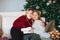 Joyful grandmother and lovely girl granddaughter in cozy knitted sweaters by Christmasmas fir tree in living room