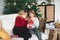 Joyful grandmother and lovely girl granddaughter in cozy knitted sweaters by Christmasmas fir tree in living room