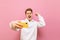 Joyful guy gamer stands with a smartphone in his hand on a pink background and is emotionally pleased to win with hand raised and