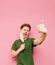 Joyful guy stands on a pink background, removes the medical mask from his face, with a happy face and shows a finger up. Emotional