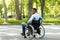 Joyful handicapped black man in wheelchair spending time at city park, full length