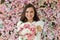 Joyful happy brunette woman with cute smile holding flower gift and posing on pink floral background. Blooming, love, 8 march