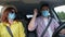 Joyful happy family have fun during joint trip by car on vacation observe safety precautions and wear medical masks to