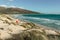 Joyful happy girl jumping on a beach on a bright summer day.Majestic view of wild sandy beach,waves and seashore.Female traveler