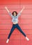 Joyful happy young woman jumping against red wall. Excited beautiful girl portrait