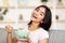 Joyful Indian lady eating granola or cereal with milk on comfy couch at home, smiling at camera