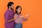 Joyful indian lovers using smartphone on orange background