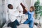 Joyful interracial couple engaging in a playful pillow fight in a bright, modern bedroom