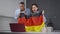 Joyful interracial couple with German flag cheering for soccer team watching online match on laptop in kitchen. Young