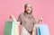 Joyful islamic woman in headscarf holding lot of bright shopper bags