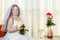 A joyful Jewish bride with her face covered with a veil with a bouquet of white roses sits in a synagogue before