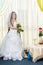 A joyful Jewish bride with her face covered with a veil and a bouquet of white roses is standing in the synagogue before