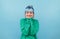 Joyful lady in green sweatshirt and blue hair is happy with a smile on her face on a blue background