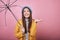 Joyful lady in striped blouse and yellow rain jacket holds hand aside as if it is dripping rain