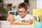 Joyful little boy sitting at the table with pencils and textbooks. Happy child pupil doing homework at the table