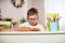 Joyful little boy sitting at the table with pencils and textbooks. Happy child pupil doing homework at the table