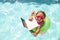 Joyful little girl swimming in pool with laptop