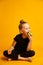 Joyful little gymnast with a carrot in his hand bites a green apple during a break, studio shot on a yellow background