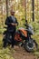 Joyful man in costume with dark motorcycle in woods