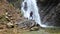 Joyful man dancing against backdrop of waterfall in mountains. Tourist enjoys active rest and vacation