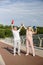 Joyful mature couple in tracksuits raises up bottles and gives five standing on city footbridge