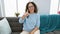 Joyful middle age hispanic woman in glasses, giving cool thumb up sign from her sofa. positive, confident expression of approval,