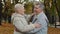 Joyful middle aged elderly couple hugging laughing standing in autumn park carefree chatting happy smiling grandma and