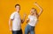 Joyful millennial guy and girl dancing over yellow studio background