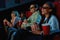 Joyful mixed race young woman wearing glasses, eating popcorn while watching movie in cinema auditorium together with