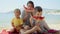 Joyful mother and her two boys, relishing sweet watermelon on the sea beach. Family vacation, summertime bliss, holiday