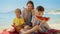 Joyful mother and her two boys, relishing sweet watermelon on the sea beach. Family vacation, summertime bliss, holiday