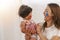 Joyful motherhood hugging own infant daughter with face painting watercolor while playful together relax in the room. Happiness