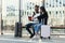 Joyful multiracial male and female mates sitting on tram stop with their suitcases and making photos of their passports.