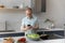 Joyful older mature man using cellphone, preparing food.