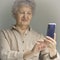 Joyful older woman smiles and takes selfie. An old woman with white hair and beige clothes