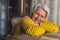 Joyful pensioner senior caucasian woman looking at camera and smiling while resting her arms on wooden table.