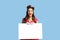Joyful pinup lady in retro style outfit holding empty advertising board with free space on blue studio background