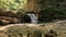 Joyful playful little girl is standing by the mountain river waterfall on background green forest. Concept of active