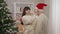 Joyful pregnant woman putting Christmas hat on man and smiling. Portrait of positive happy Caucasian wife enjoying New