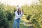 Joyful pretty young woman in warm hat photography beautiful christmas trees during walking among forestry plantings.